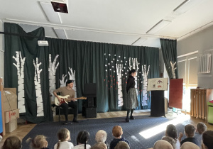 Pan gra na gitarze, dzieci siedzą a pani im opowiada.