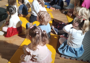 Widać siedzące i przyglądające się czemuś dzieci.