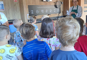 Dzieci stoją tyłem, słuchają co mówi do nich pani.