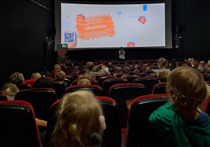 Dzieci siedzą w kinie, w głębi widać ekran z napisem Dziecięca Akademia Bezpieczeństwa