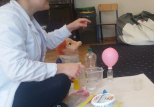 Na dywanie postawione różne plastikowe pudełka i różowy balon.