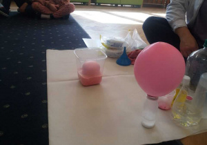 Widać coraz większy różowy balon i w pojemnikach różne substancje.